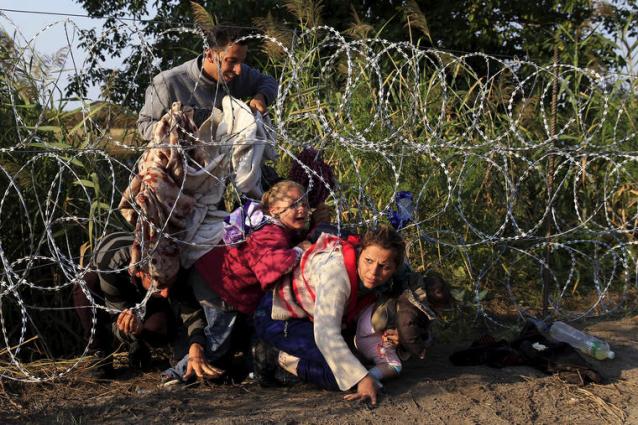 Syrian migrants cross under a fence as they enter Hungary at the border with Serbia, near Roszke, August 27, 2015. Hungary made plans on Wednesday to reinforce its southern border with helicopters, mounted police and dogs, and was also considering using the army as record numbers of migrants, many of them Syrian refugees, passed through coils of razor-wire into Europe. REUTERS/Bernadett Szabo TPX IMAGES OF THE DAY - RTX1PU25